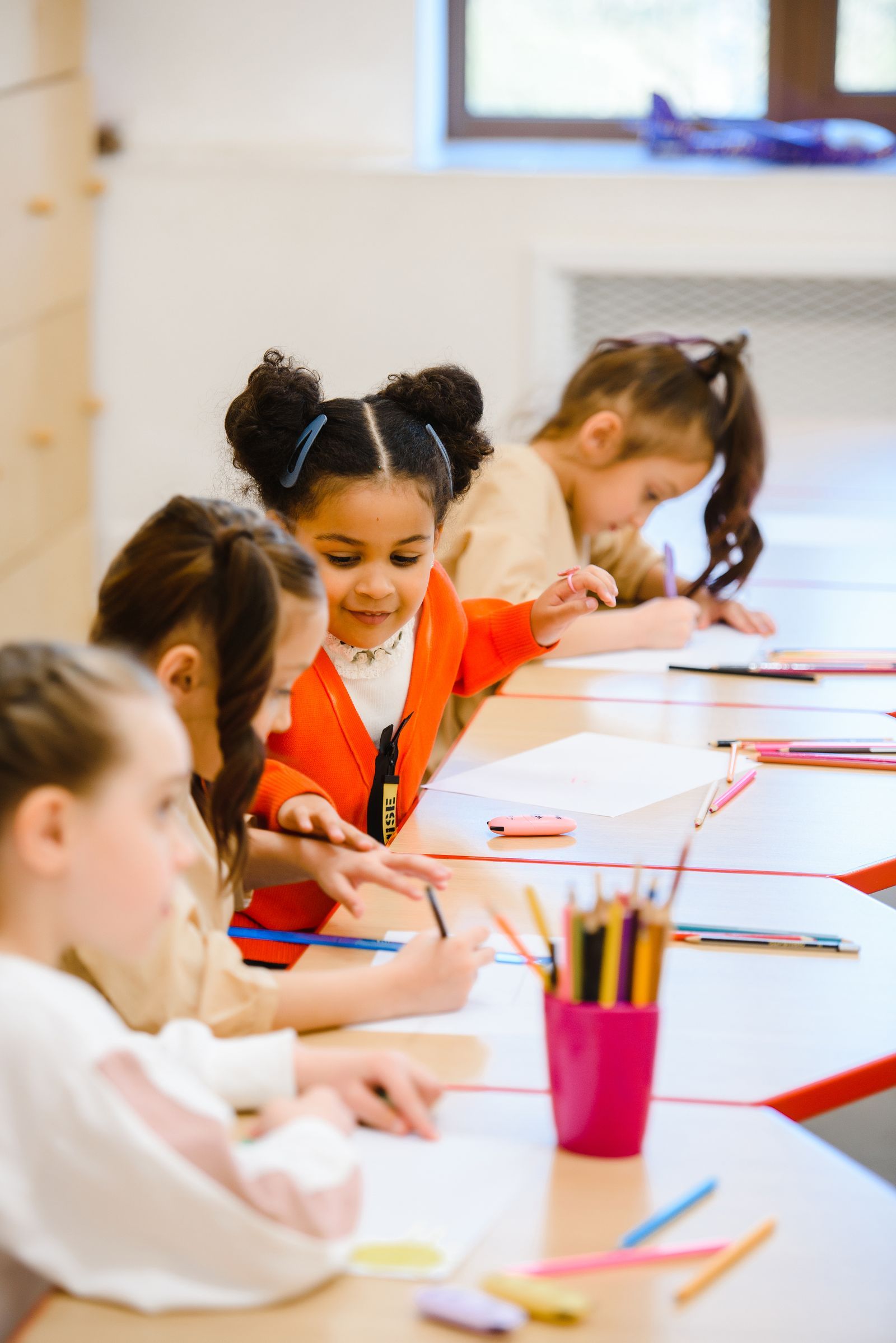 Preschool children drawing with colored pencils at a classroom table