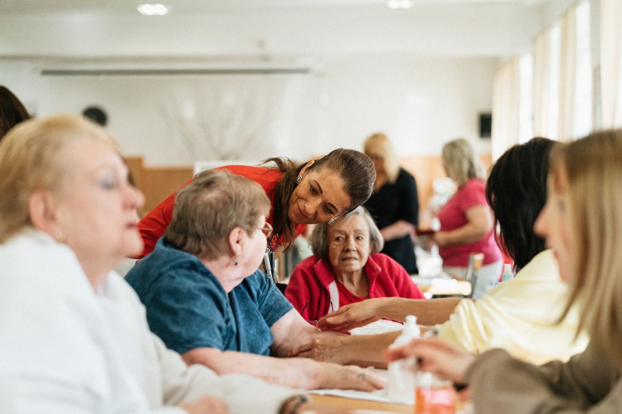 A caregiver leaning in to talk with older adults at a table in an adult day center